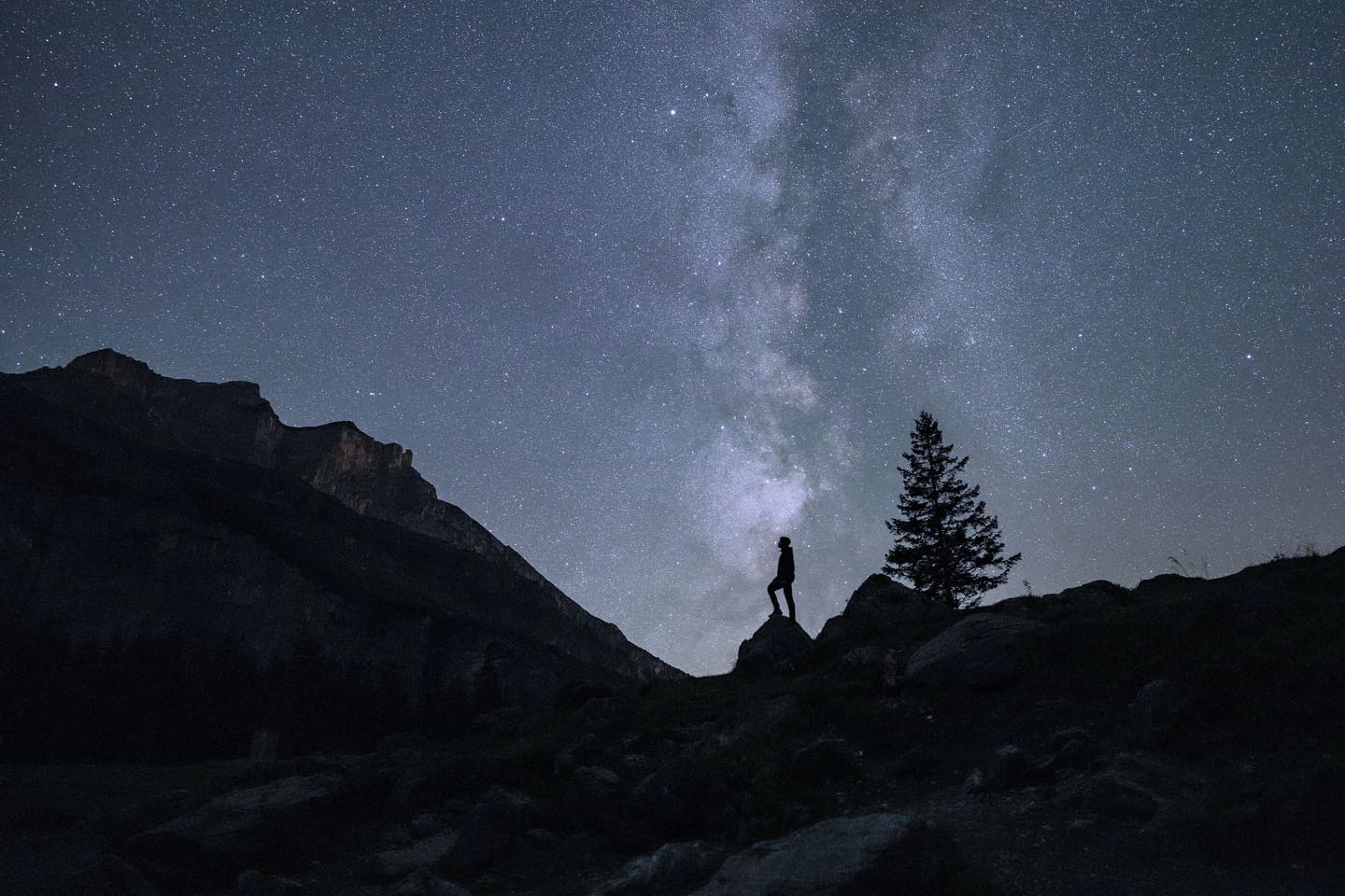 Una persona, in piedi su una roccia, osserva la Via Lattea sopra le montagne.