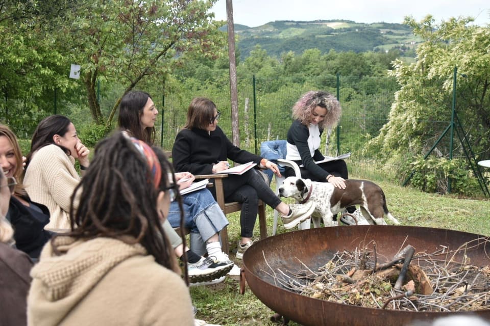 Una lezione all’aperto: le partecipanti sedute in cerchio sul prato, con un cane che passa tra le sedie.
