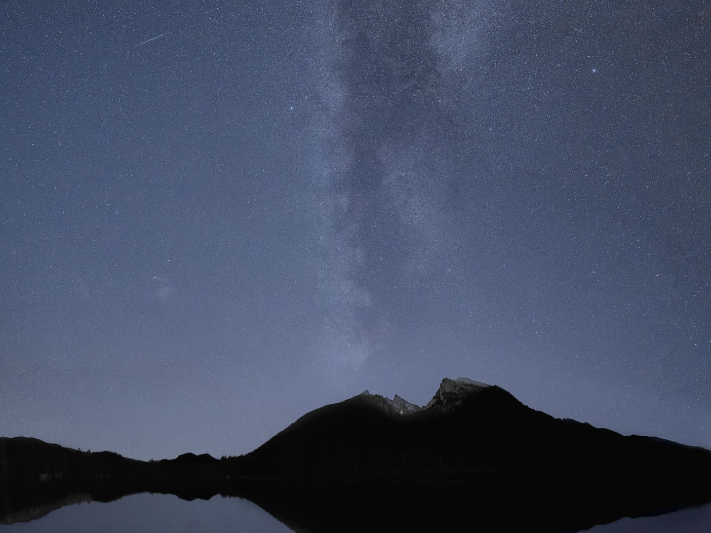 La Via Lattea sopra una montagna che si riflette nell’acqua ferma di un lago.